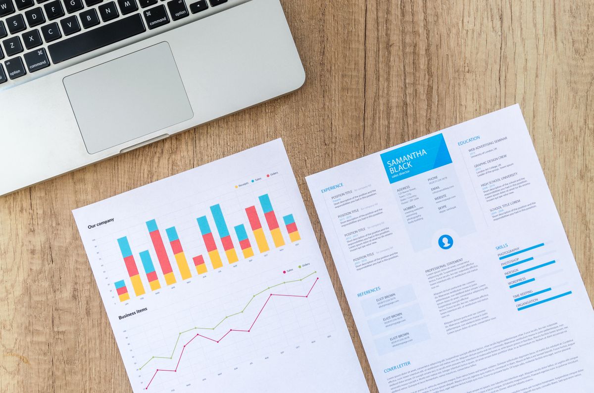 A resume and performance charts beside a laptop